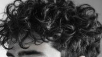 Man with curly hair wearing a black shirt against a neutral background
